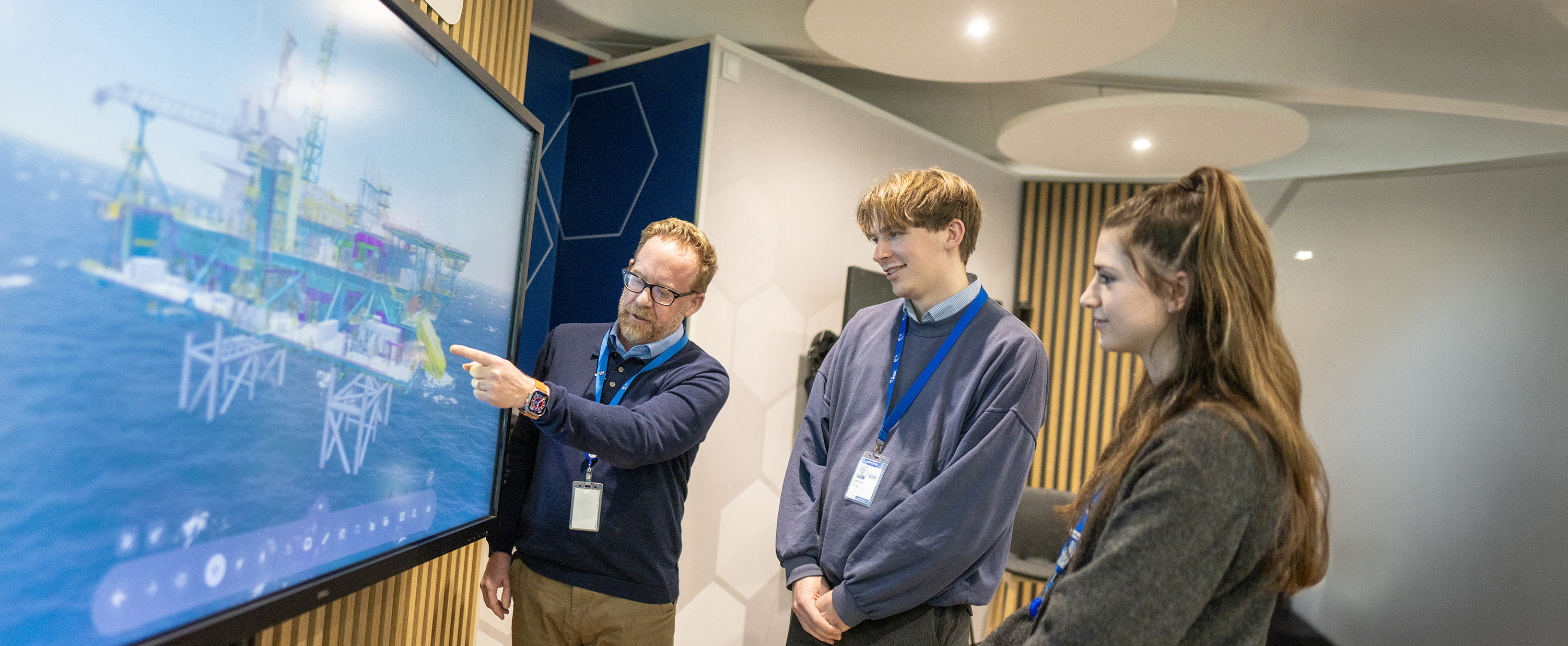 A KBR employee presenting a 3D offshore platform model on screen to two student interns